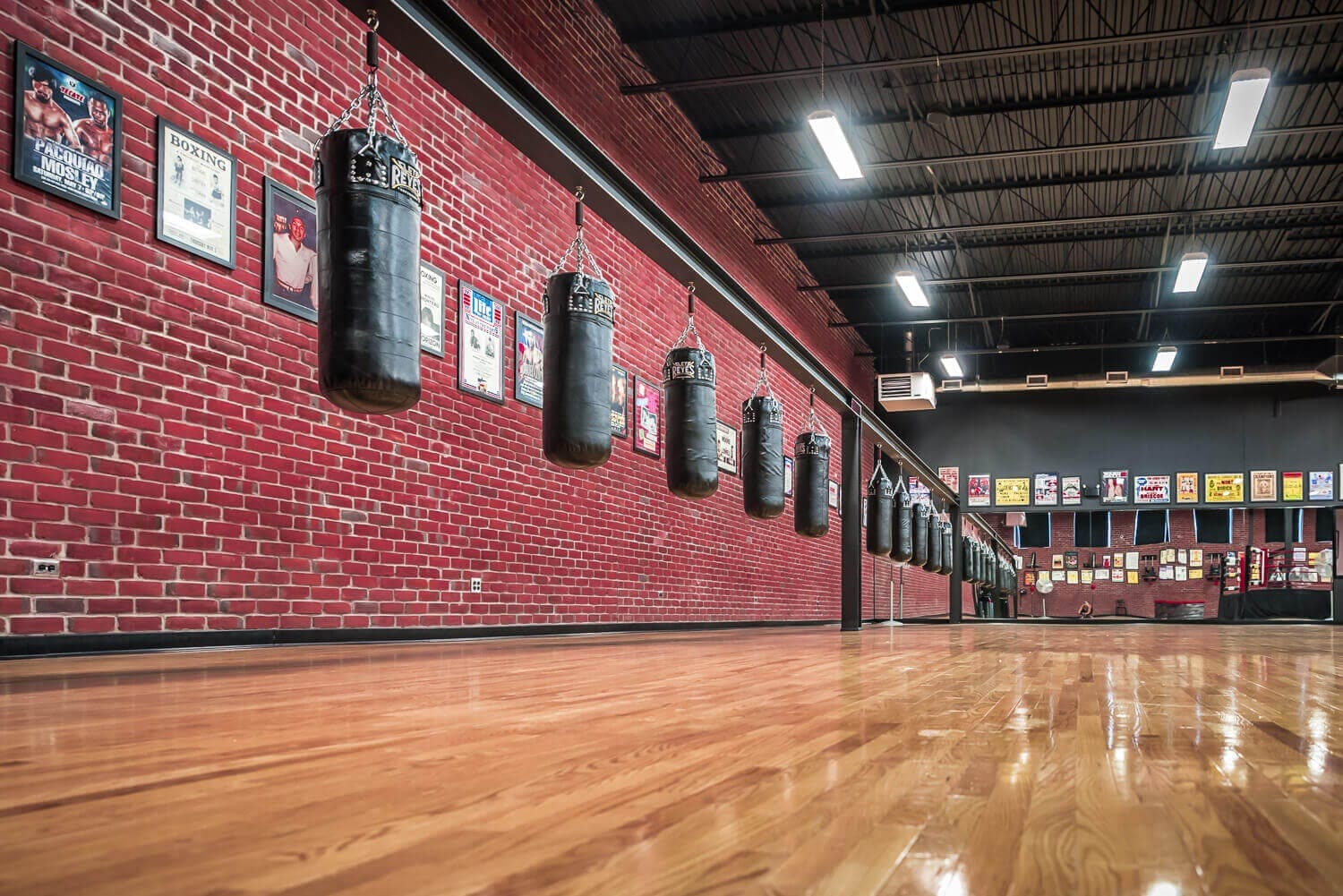 The heavy bag row at West End Athletic Club — brick walls, hardwood floor, championship posters